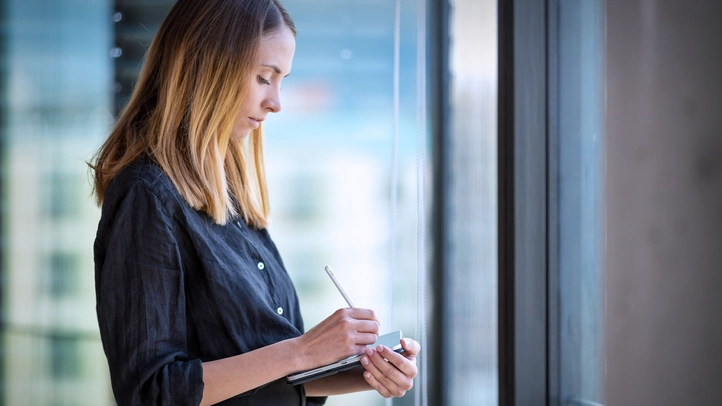 UX Designerin Nicole Lössner arbeitet auf ihrem Tablet an einem Prototypen. Sie steht im Büro an einer vollverglasten Fensterfront.