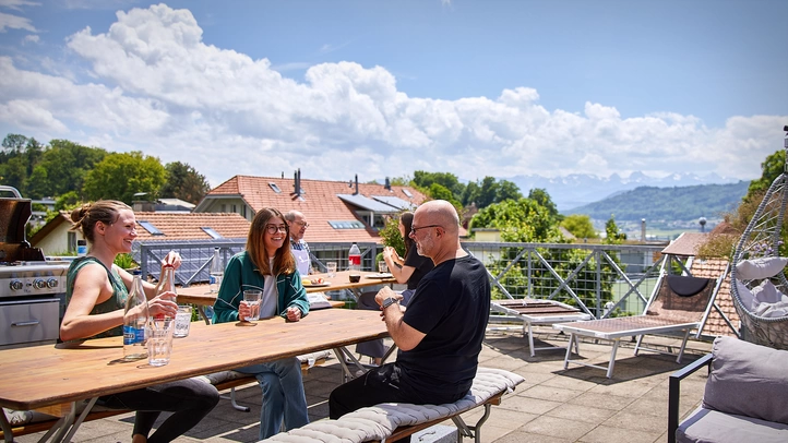 Three people talking on a roof terrace. The Alps in the background.