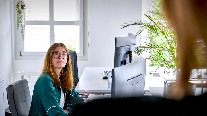 Frau an ihrem Arbeitsplatz reagiert auf Person im Vordergrund