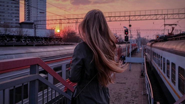 Eine Frau wartet im Sonnenuntergang am Bahnhof auf ihren Zug.