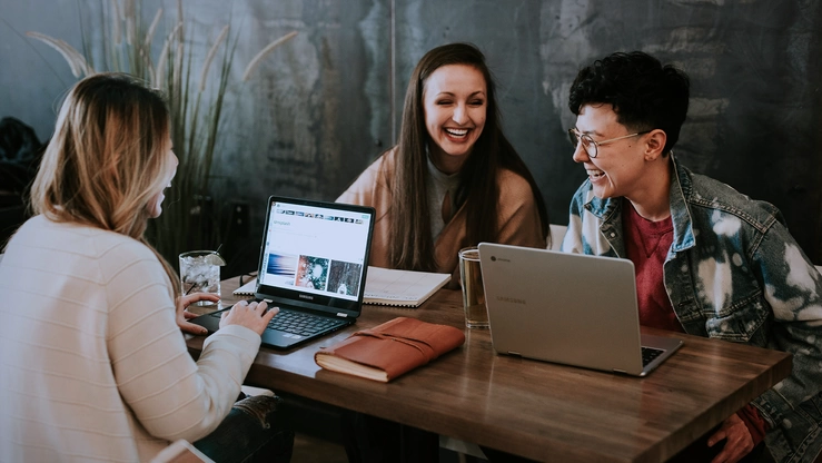 Three women confer at a table.