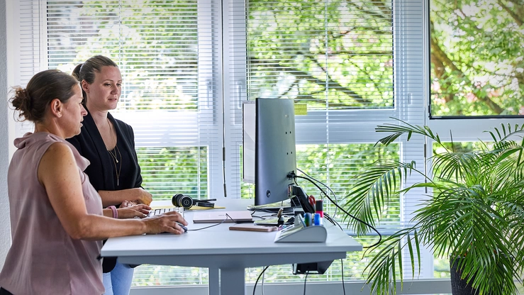 Zwei Kolleginnen stehend an einem Schreibtisch