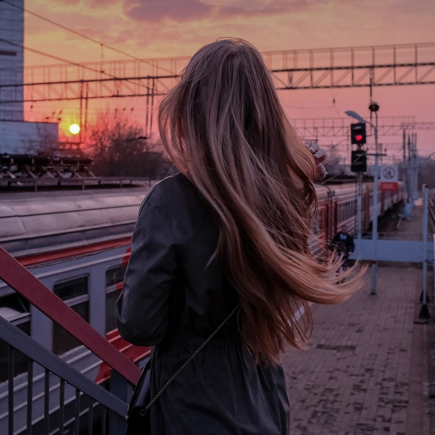 Eine Frau wartet im Sonnenuntergang am Bahnhof auf ihren Zug.