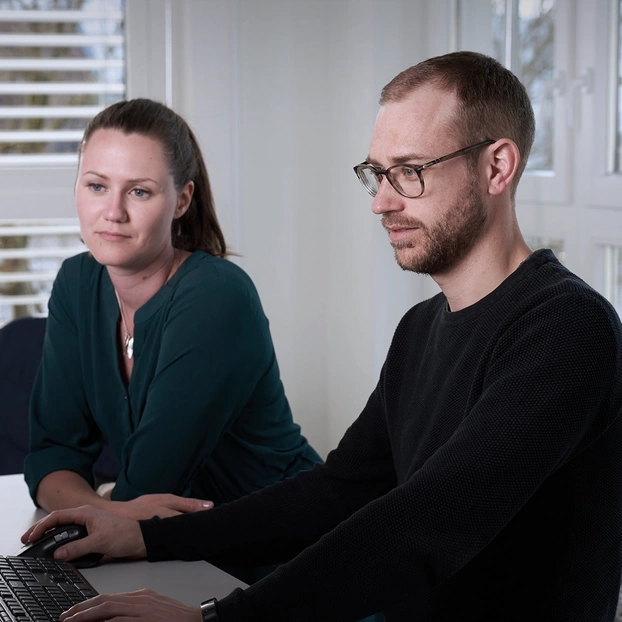 Zwei Mitarbeitende hinter einem PC-Screen