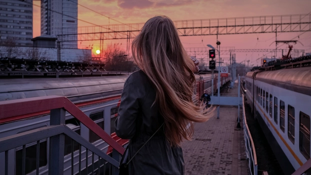 Eine Frau wartet im Sonnenuntergang am Bahnhof auf ihren Zug.