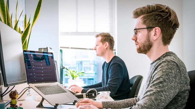 Deux personnes travaillent sur un poste de travail informatique.