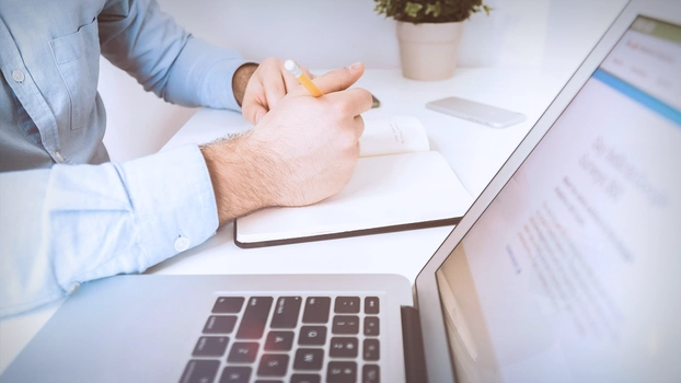 Une main et un ordinateur portable sur une table.